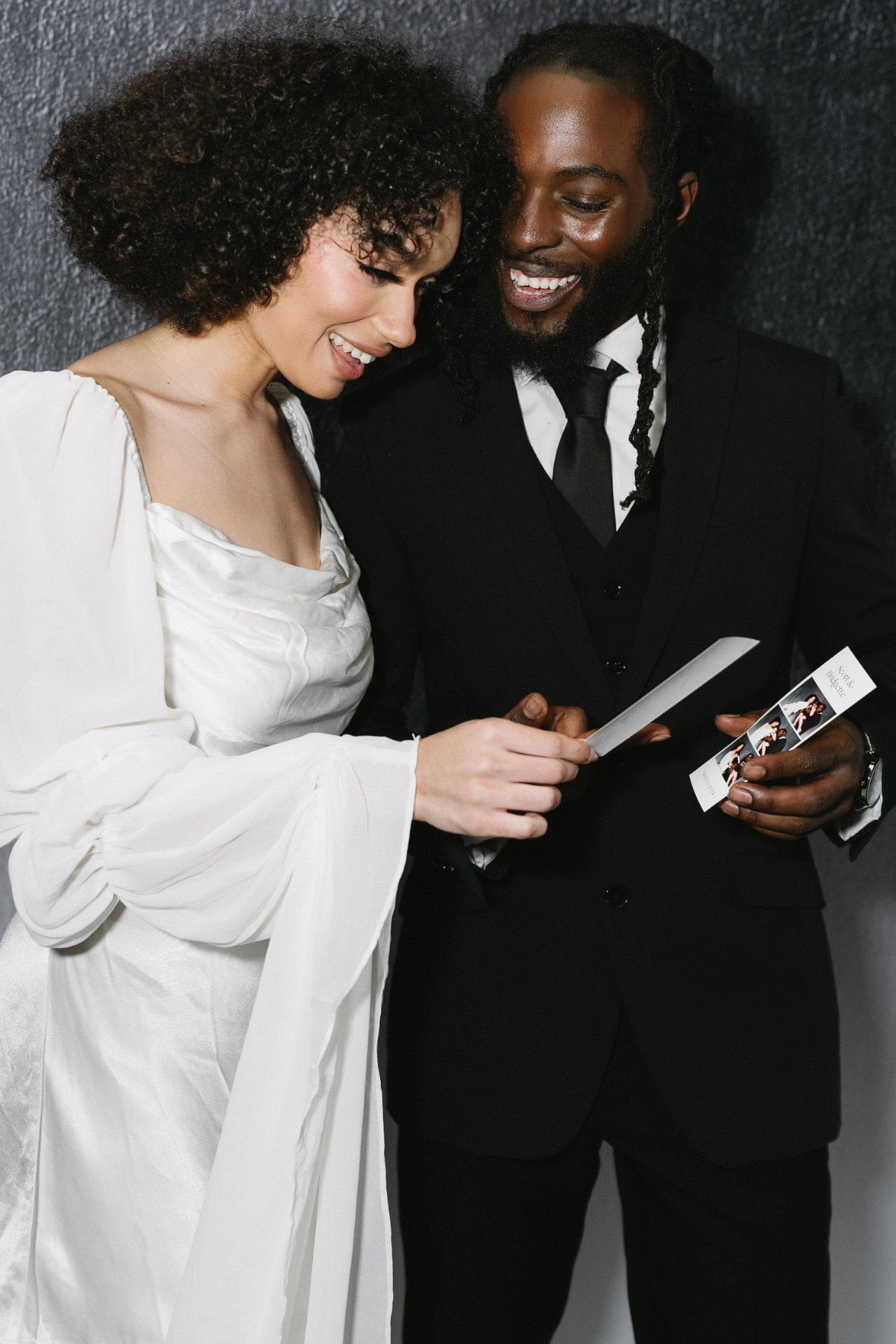 A couple in formal attire smiling at their printed photo strip from the booth