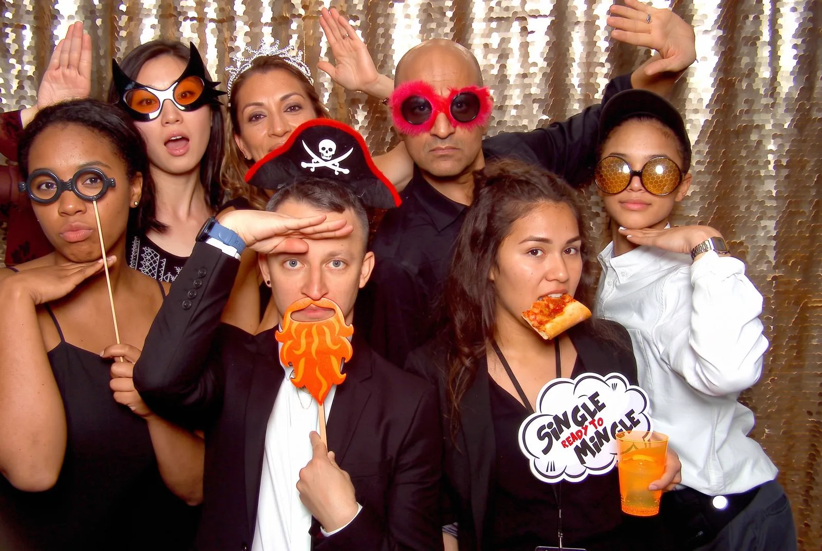 A group of guests laughing with props in front of a shimmering photo booth backdrop
